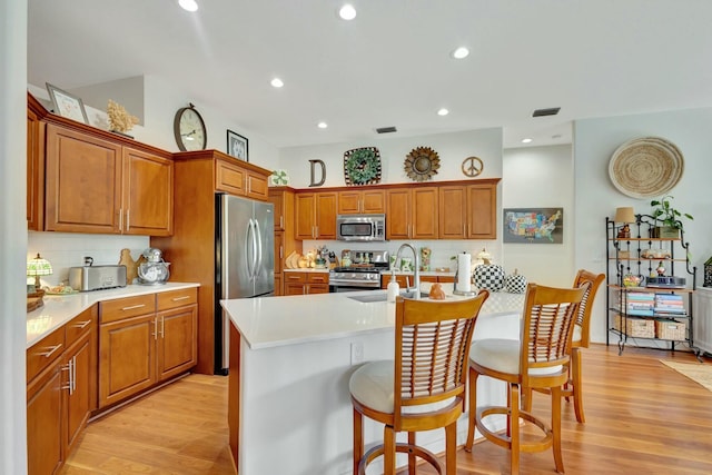 kitchen with appliances with stainless steel finishes, a kitchen island with sink, sink, light hardwood / wood-style flooring, and a breakfast bar area