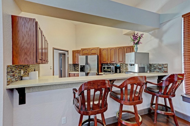 kitchen featuring kitchen peninsula, tasteful backsplash, stainless steel appliances, dark wood-type flooring, and a breakfast bar area