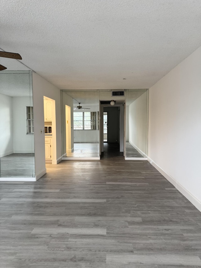 spare room with a textured ceiling, wood finished floors, visible vents, a ceiling fan, and baseboards