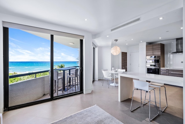 kitchen featuring a kitchen breakfast bar, wall chimney exhaust hood, stainless steel double oven, a water view, and hanging light fixtures