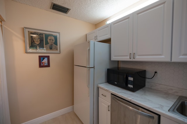 kitchen featuring dishwasher, white fridge, a textured ceiling, decorative backsplash, and white cabinets