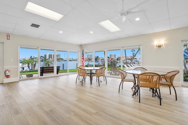 dining room featuring ceiling fan, a drop ceiling, a water view, and light wood-type flooring