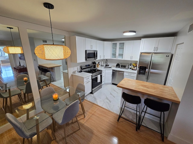 kitchen featuring a breakfast bar, stainless steel appliances, pendant lighting, white cabinets, and light hardwood / wood-style floors