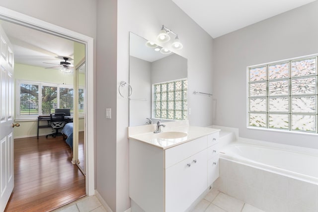 bathroom featuring hardwood / wood-style floors, vanity, a relaxing tiled tub, and ceiling fan