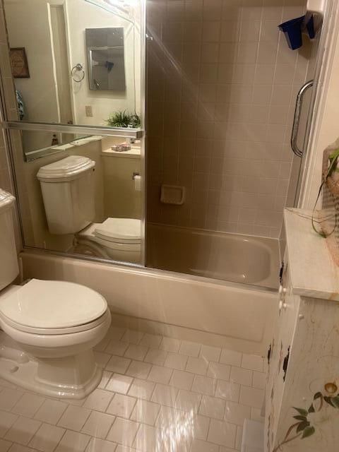 bathroom featuring tile patterned flooring, combined bath / shower with glass door, and toilet