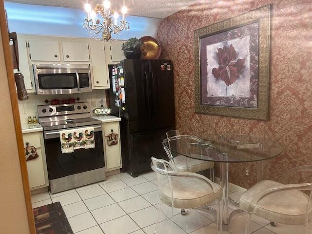 kitchen with appliances with stainless steel finishes, a textured ceiling, light tile patterned floors, an inviting chandelier, and white cabinetry