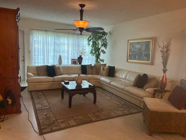 living room featuring ceiling fan, light hardwood / wood-style flooring, and a textured ceiling