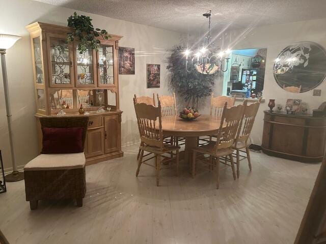 dining room with light wood-type flooring, a textured ceiling, and an inviting chandelier