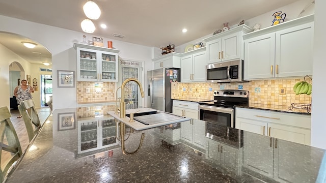 kitchen featuring backsplash, dark stone counters, stainless steel appliances, sink, and white cabinetry