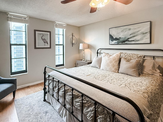 bedroom featuring multiple windows, ceiling fan, wood-type flooring, and a textured ceiling