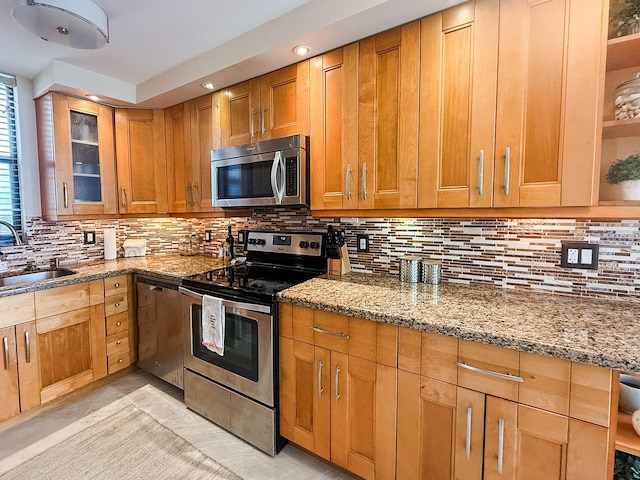 kitchen with backsplash, stainless steel appliances, light stone counters, and sink