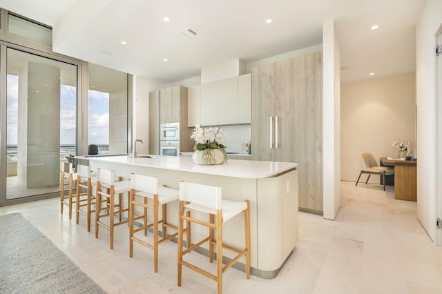 kitchen featuring a kitchen breakfast bar, white appliances, a kitchen island with sink, sink, and white cabinetry