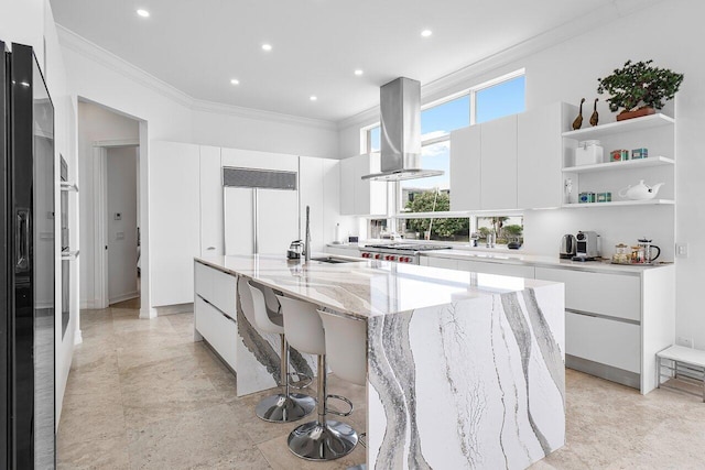 kitchen featuring a large island with sink, light stone countertops, white cabinets, and range hood