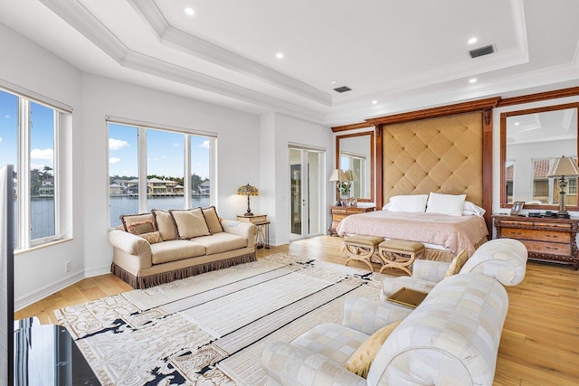 bedroom with light hardwood / wood-style floors, a water view, crown molding, and a tray ceiling