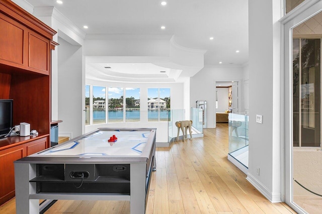 rec room featuring a raised ceiling, a water view, crown molding, and light hardwood / wood-style floors