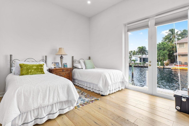 bedroom with access to exterior, hardwood / wood-style floors, and a water view