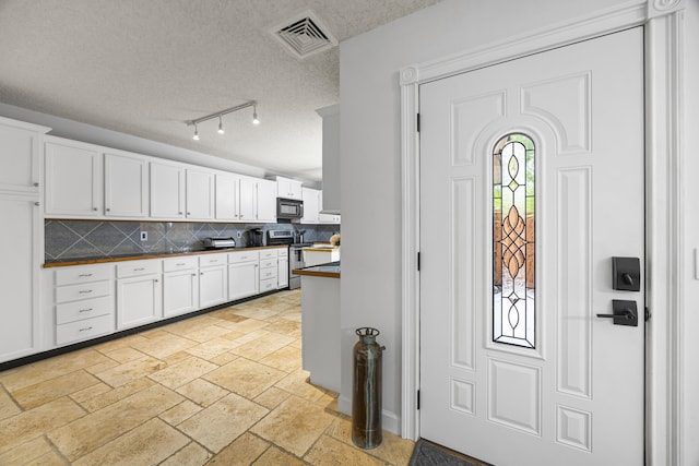 kitchen with white cabinets, decorative backsplash, a textured ceiling, and stainless steel range with electric stovetop