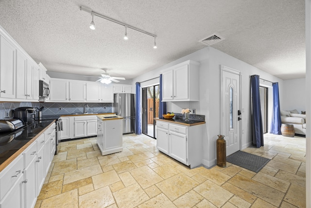 kitchen with decorative backsplash, a textured ceiling, stainless steel appliances, ceiling fan, and white cabinetry