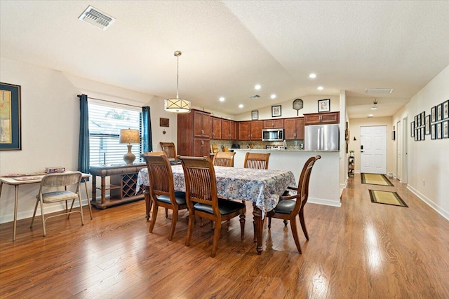 dining room with a textured ceiling, wood-type flooring, and lofted ceiling