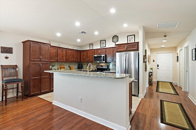 kitchen with light hardwood / wood-style flooring, backsplash, lofted ceiling, a center island with sink, and appliances with stainless steel finishes