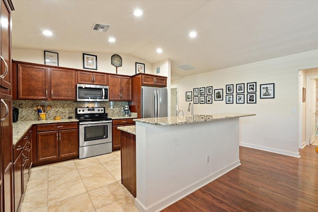 kitchen featuring a center island, stainless steel appliances, light stone counters, light hardwood / wood-style flooring, and vaulted ceiling