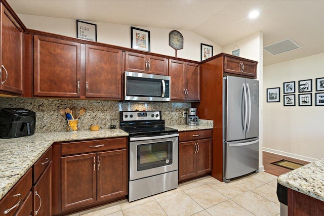 kitchen featuring light stone countertops, backsplash, vaulted ceiling, light tile patterned floors, and appliances with stainless steel finishes