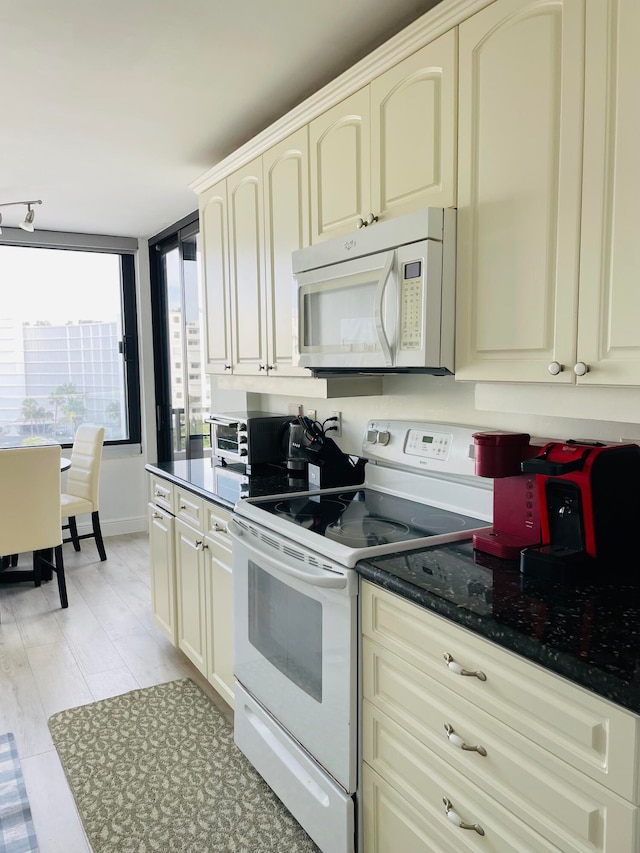 kitchen with cream cabinetry, white appliances, light hardwood / wood-style flooring, and dark stone countertops