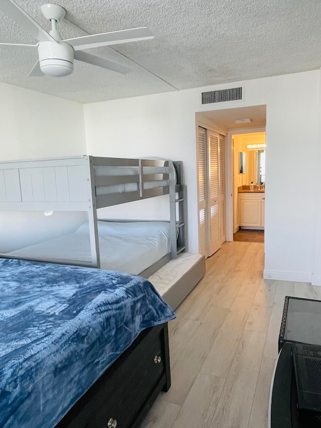 bedroom featuring connected bathroom, ceiling fan, light hardwood / wood-style flooring, and a textured ceiling