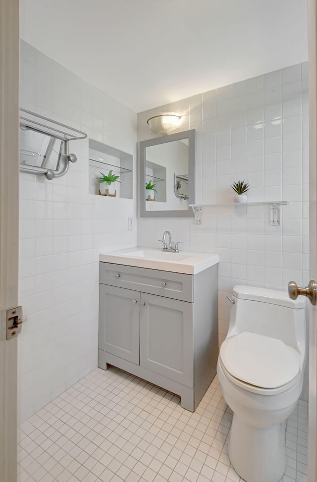 bathroom with toilet, vanity, tile patterned floors, and tile walls