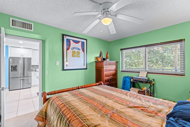 bedroom with a textured ceiling, ceiling fan, light tile patterned floors, and stainless steel refrigerator with ice dispenser