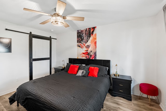 bedroom with ceiling fan, light hardwood / wood-style floors, and a barn door