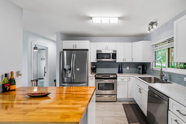 kitchen with wooden counters, appliances with stainless steel finishes, tasteful backsplash, sink, and white cabinets