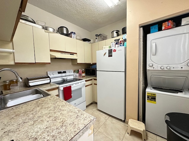 kitchen with sink, cream cabinetry, stacked washer and dryer, a textured ceiling, and white appliances