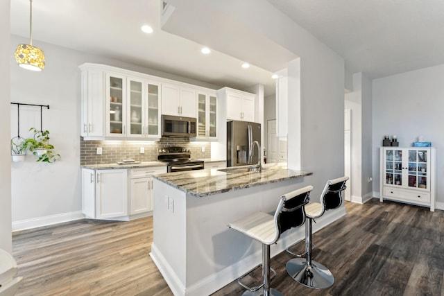 kitchen featuring decorative backsplash, appliances with stainless steel finishes, wood finished floors, light stone countertops, and a sink