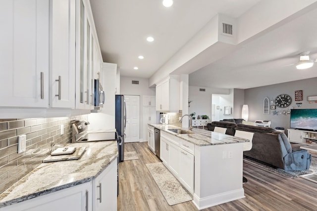 kitchen featuring light wood-style flooring, appliances with stainless steel finishes, open floor plan, white cabinetry, and a sink