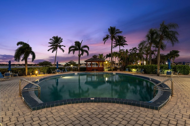 pool at dusk with a patio area, a gazebo, and a community pool