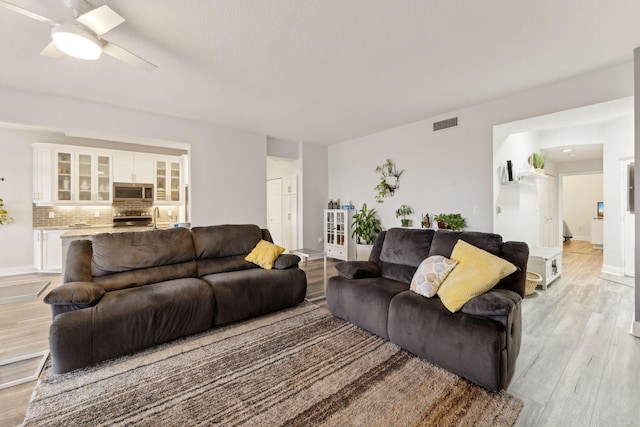 living area with light wood-style floors, visible vents, ceiling fan, and baseboards