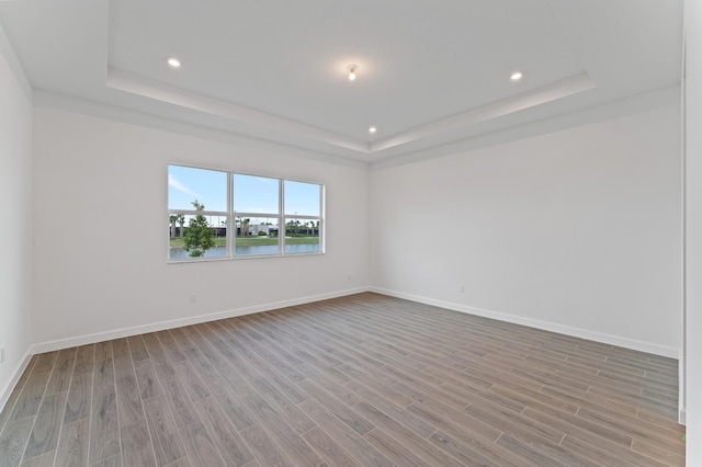 spare room with light hardwood / wood-style flooring, a raised ceiling, and a water view