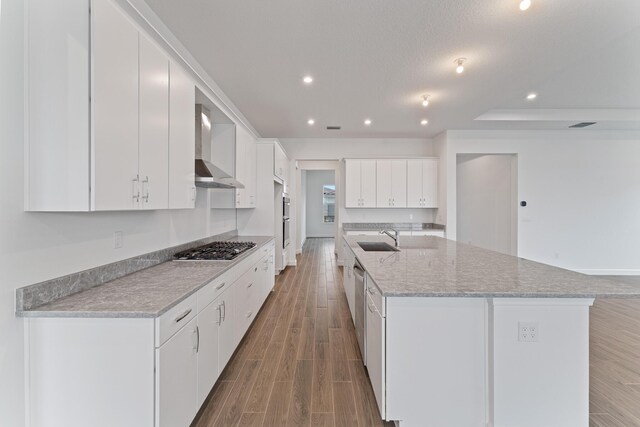 kitchen with sink, white cabinetry, stainless steel appliances, an island with sink, and wall chimney exhaust hood