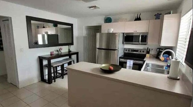 kitchen with white cabinetry, sink, stainless steel appliances, kitchen peninsula, and light tile patterned floors