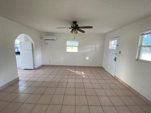 tiled spare room with ceiling fan and a wall unit AC