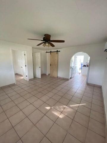 tiled empty room with a barn door and ceiling fan