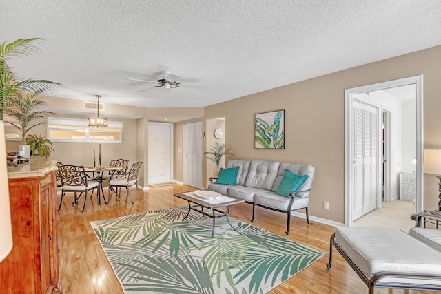 living room with ceiling fan with notable chandelier, light hardwood / wood-style floors, and a textured ceiling