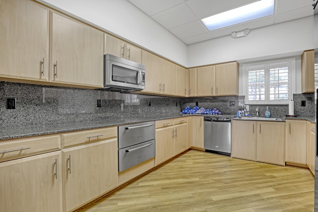 kitchen with appliances with stainless steel finishes, dark stone counters, light hardwood / wood-style floors, and light brown cabinetry