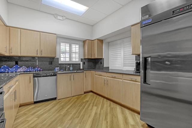 kitchen featuring dark stone counters, decorative backsplash, light brown cabinetry, appliances with stainless steel finishes, and light hardwood / wood-style floors