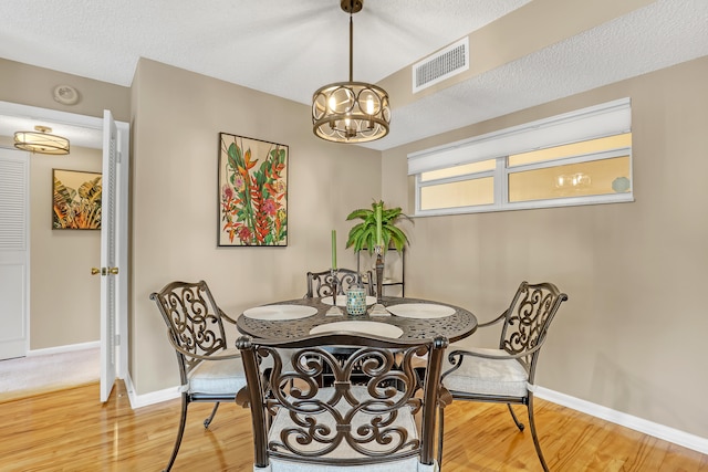 dining space featuring a textured ceiling, a notable chandelier, and hardwood / wood-style flooring