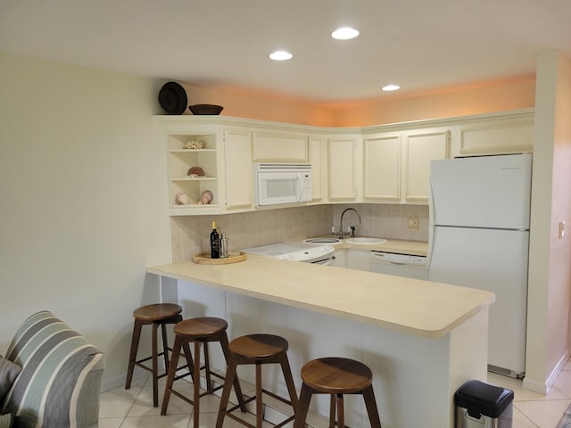 kitchen featuring light tile patterned floors, kitchen peninsula, decorative backsplash, white appliances, and a kitchen breakfast bar