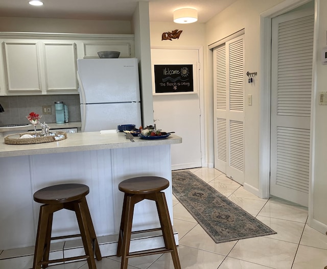 kitchen featuring a kitchen bar, decorative backsplash, white cabinets, and white refrigerator