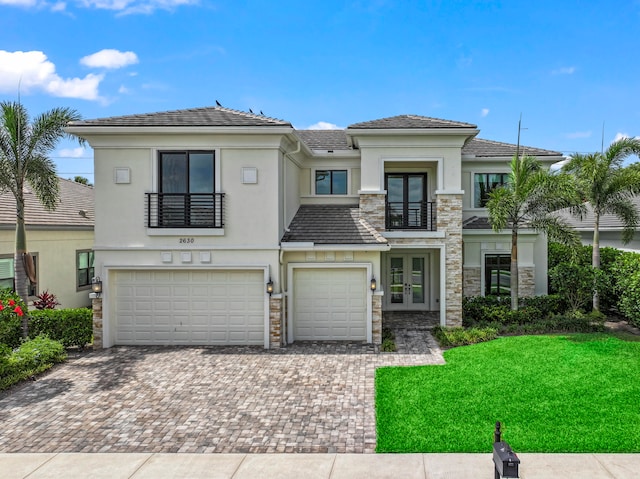 view of front facade featuring a front lawn, a garage, a balcony, and french doors