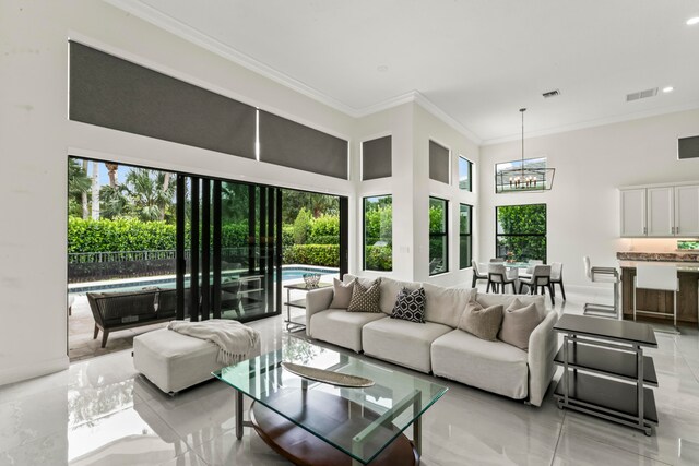 living room featuring a wealth of natural light, a towering ceiling, a notable chandelier, and ornamental molding